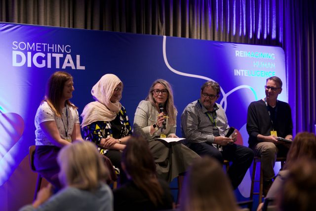 A photo shows four panelists sitting on a stage on stools during a panel discussion. 