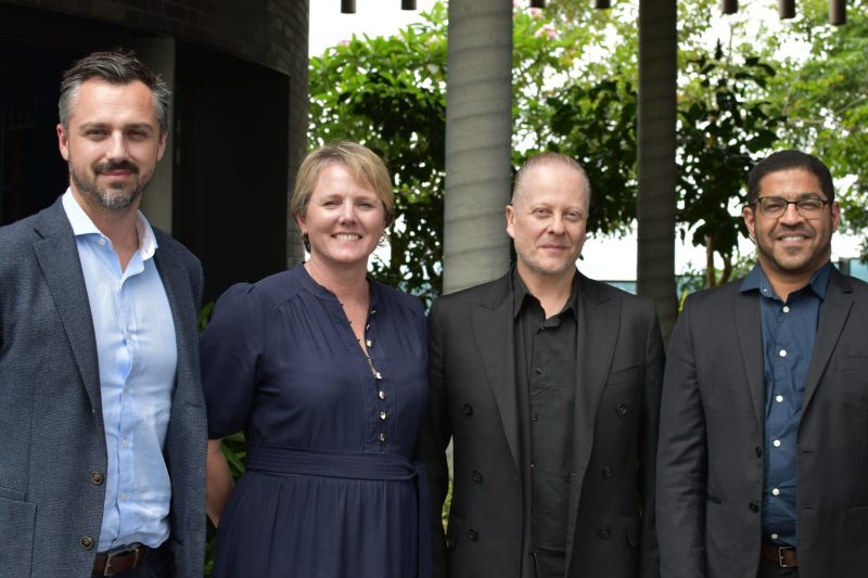 A group of four individuals poses together in front of a large building, showcasing a friendly atmosphere.