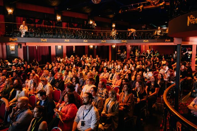 A photo of a seated audience who appear to be looking at a stage.