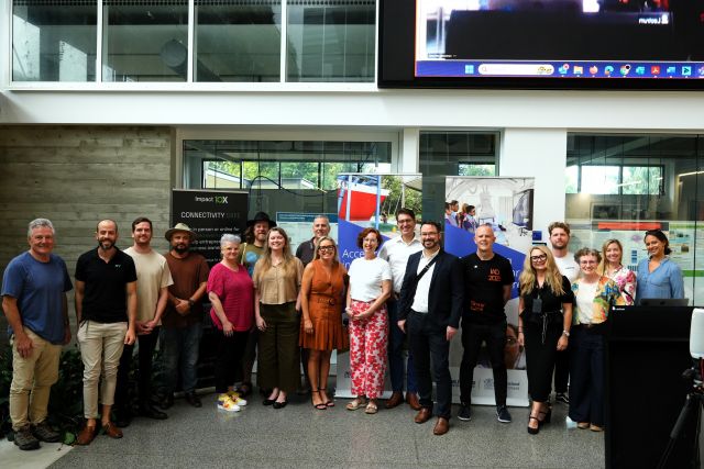 A diverse group of people stands together in front of a large screen displaying information or visuals. 